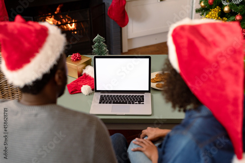 Back view of african american couple wearing santa hats, using laptop with copy space on screen