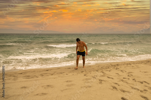 young Caucasian man coming out of the sea and walking on the sand of the beach on the shore