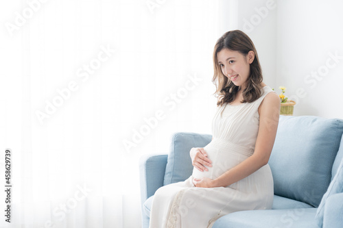 笑顔でお腹を撫でる若い妊婦（妊娠・マタニティ）