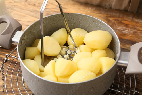 Pot with boiled potatoes and masher on table