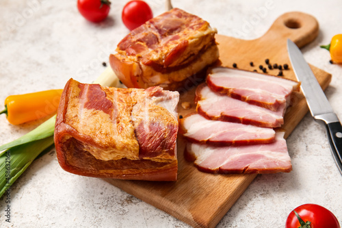 Wooden board with tasty smoked bacon on light background