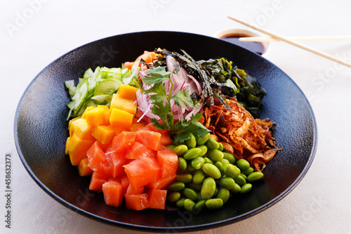 healthy poke bowl with edamame, salmon, wakame seaweed, mango, radish, cucumber, onion and rice served with sweet soy sauce, japanese food speciality