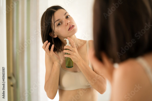 A young girl applies a balm, a care oil to her hair by the mirror