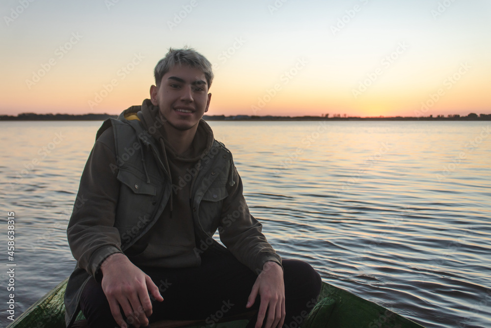 Young smiling man riding in a boat with the sunset in the background.