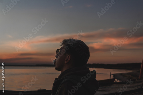 Young man making a gum balloon with his mouth while watching the sunset on the abandoned beach.