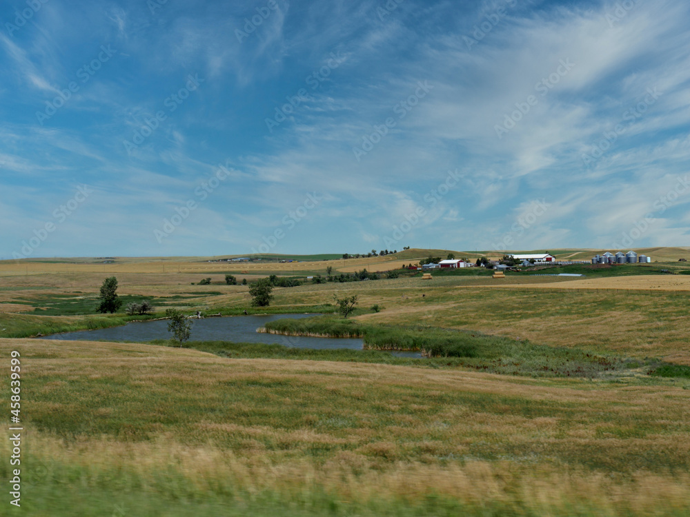 Roadside view of a small pond with distant structures along Highway 44 in South Dakota, USA.
