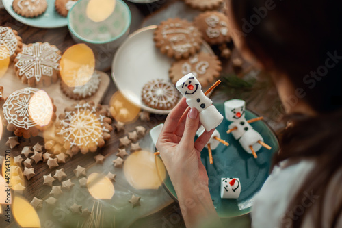 Mom and children decorate Christmas gingerbread at home. A boy and a girl paint with cornets with sugar icing on cookies. New Year's decor, branches of a Christmas tree.