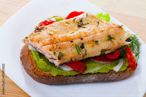 Image of tasty sandwich with trout, guacamole, red pepperand greens at plate