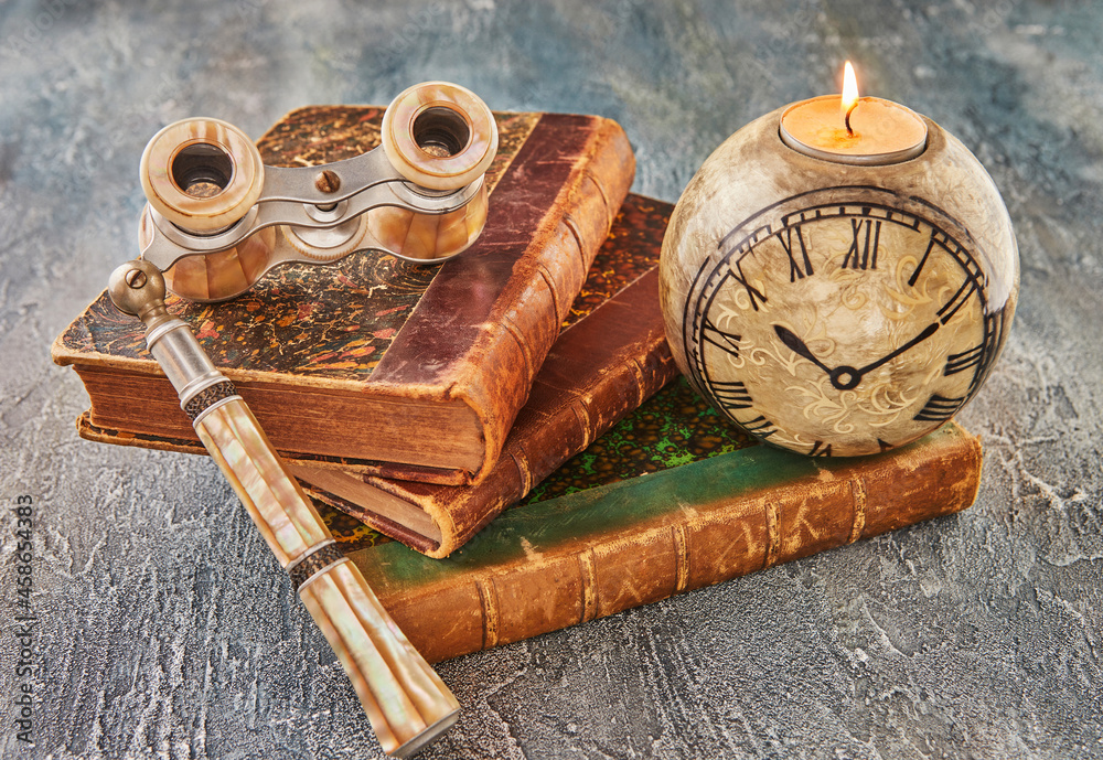 Still life with antique books, theatrical binoculars and candles in the shape of clock