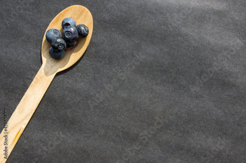 Flat lay of recycled spoon and juicy fresh blueberries on rough table. Space for text. Isolated ripe sweet bilberry fruits in eco spoon on black background. Copyspace. Healthy raw vegetarian food 