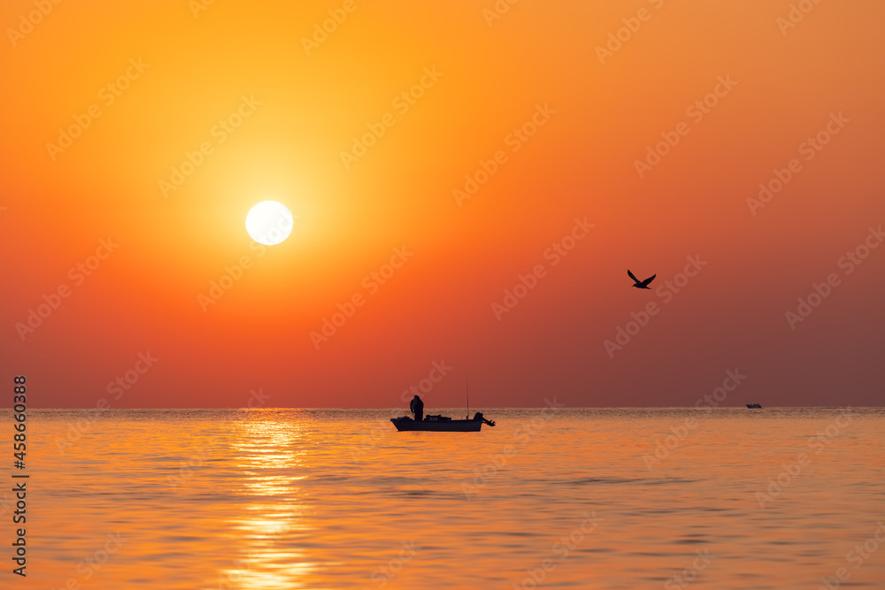 Fototapeta premium Silhouette of fisherman in a boat and norning sunrise