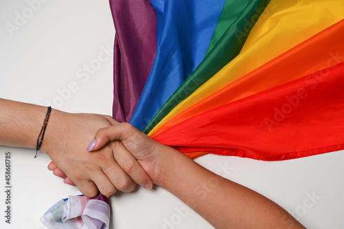Two women LGBT lesbian hands are holding each other over LGBT pride flag.