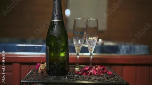 Push out shot of a cold bottle of champagne with two glasses rose petals and candles by a jacuzzi. Romantic set up for a date in a cabin. Love and couples conceptn a cabin. Love and couples concept photo