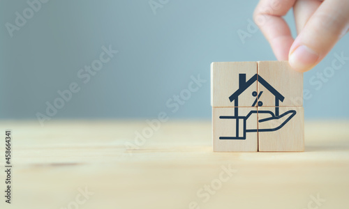 Home loan, mortgage and buy a real estate concept. Hand puts the wooden cube with icon of hands holding house model in grey background and copy space. Banner for home buying, loan and insurance