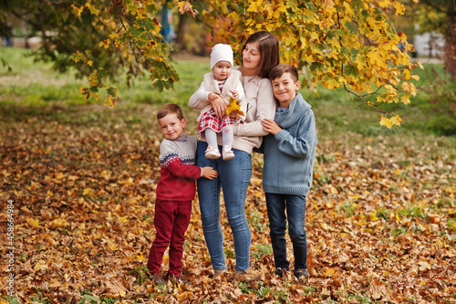 Happy family at autumn leaves park. Mother with three kids.