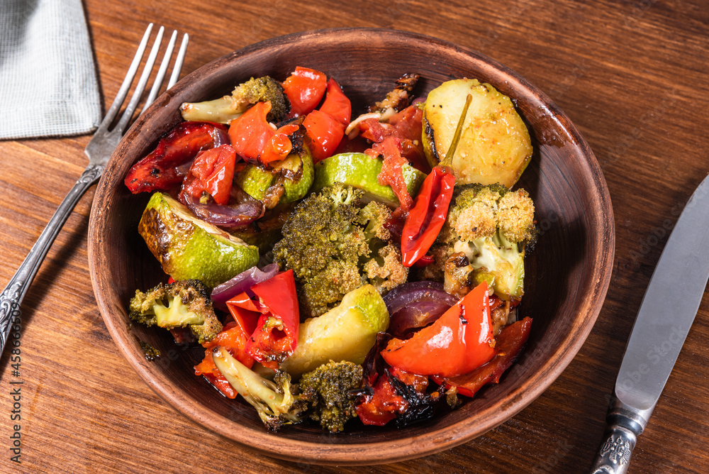 Baked vegetables, broccoli, tomatoes, peppers and zucchini in a plate on the table, close-up - vegetarian healthy cuisine Baked vegetables, broccoli, tomatoes, peppers and zucchini in a plate on the table, close-up - vegetarian healthy cuisine