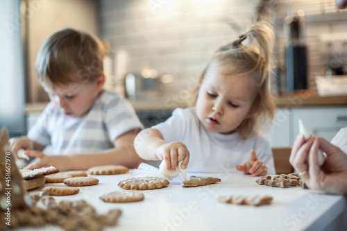 children decorate Christmas gingerbread at home. A boy and a girl paint with cornets with sugar icing on cookies. New Year's decor, branches of a Christmas tree.