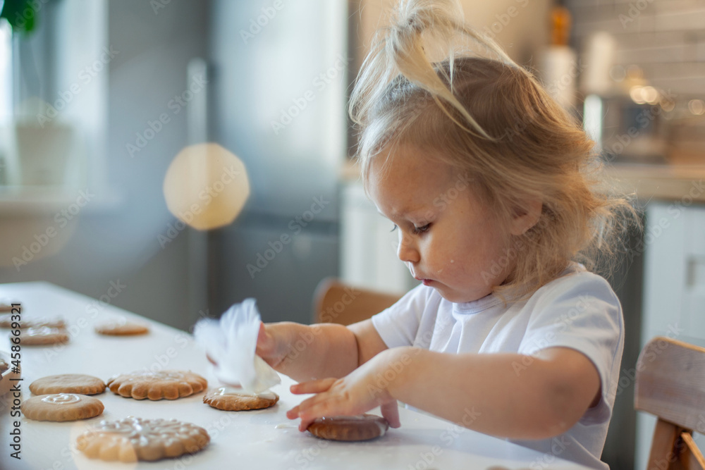 Little cute girl decorates gingerbread with sugar icing. Preparation for Christmas concept.