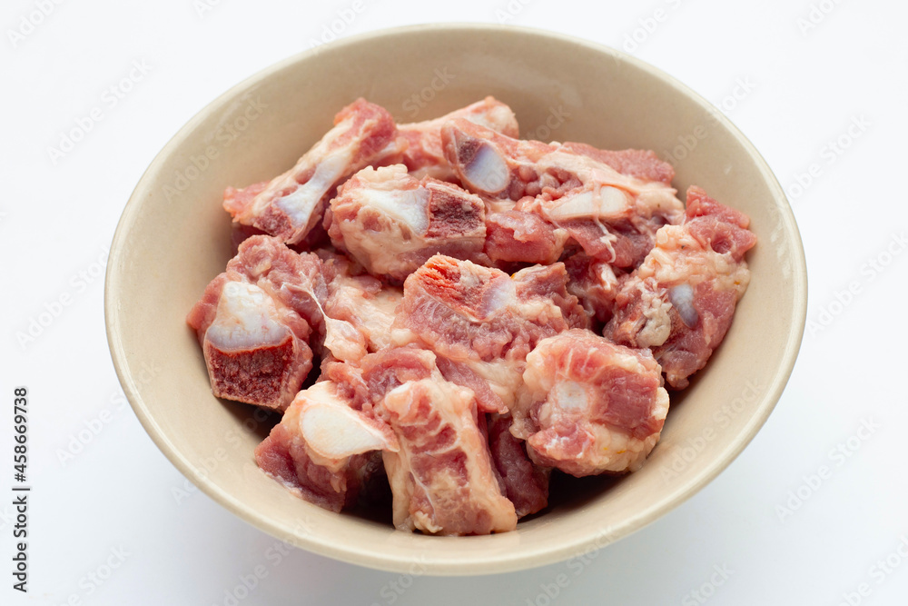 Raw pork ribs in bowl on white background.