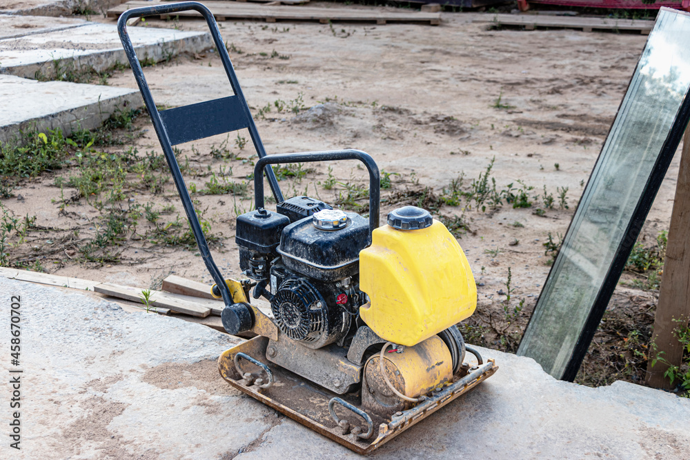 Vibratory rammer with vibrating plate on a construction site. Compaction of the soil before laying paving slabs. Close-up.