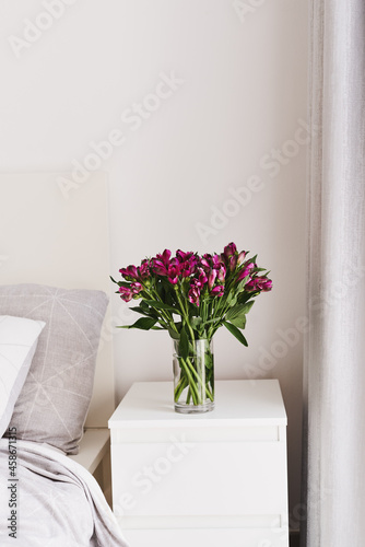 Alstroemeria flowers in a vase on a white bedside table. Simple and cozy bedroom decor. Minimal style. Fresh flowers in home decor and interior design