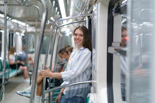 Cheerful young girl inside metro carriage student return home after successful exam in university. Smiling female lean at door in underground happy to travel subway after lockdown without restrictions
