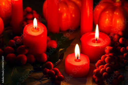 Candlelight in the dark. Halloween decor. Autumn orange pumpkins, red berries, dried oak leaves and three burning candles