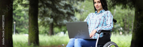 Foto Young woman in wheelchair working on laptop in park