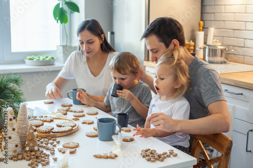 A cheerful family decorates Christmas gingerbread, drinks tea and has fun. Stylish home kitchen.