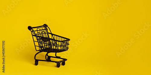 Black shopping cart isolated on a vibrant yellow background. Creative Black Friday concept. Sale or promotion banner. Minimal retail store idea.