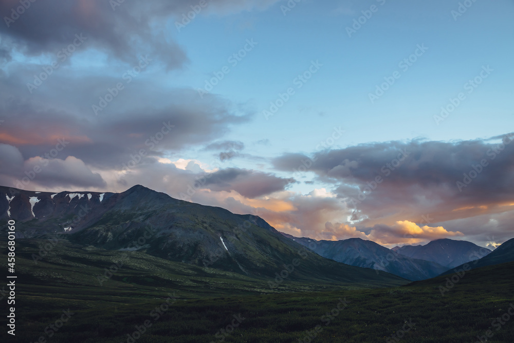 Beautiful mountain scenery with golden dawn light in cloudy sky. Scenic mountain landscape with illuminating color in sunset sky. Silhouettes of mountains on sunrise. Gold illuminating sunlight in sky