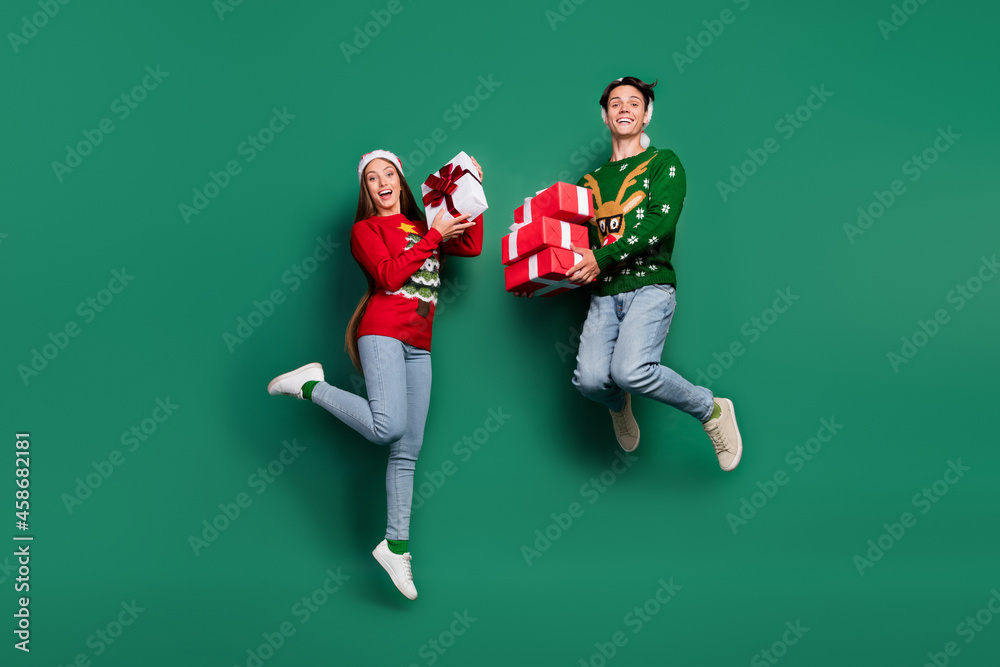 Photo of crazy carefree couple hold present boxes jump wear ugly sweater isolated green color background