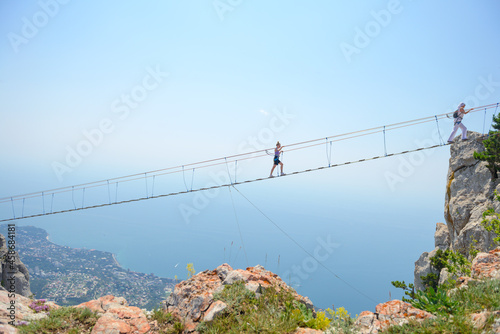 Tourists walk along the hanging bridge over the cliff