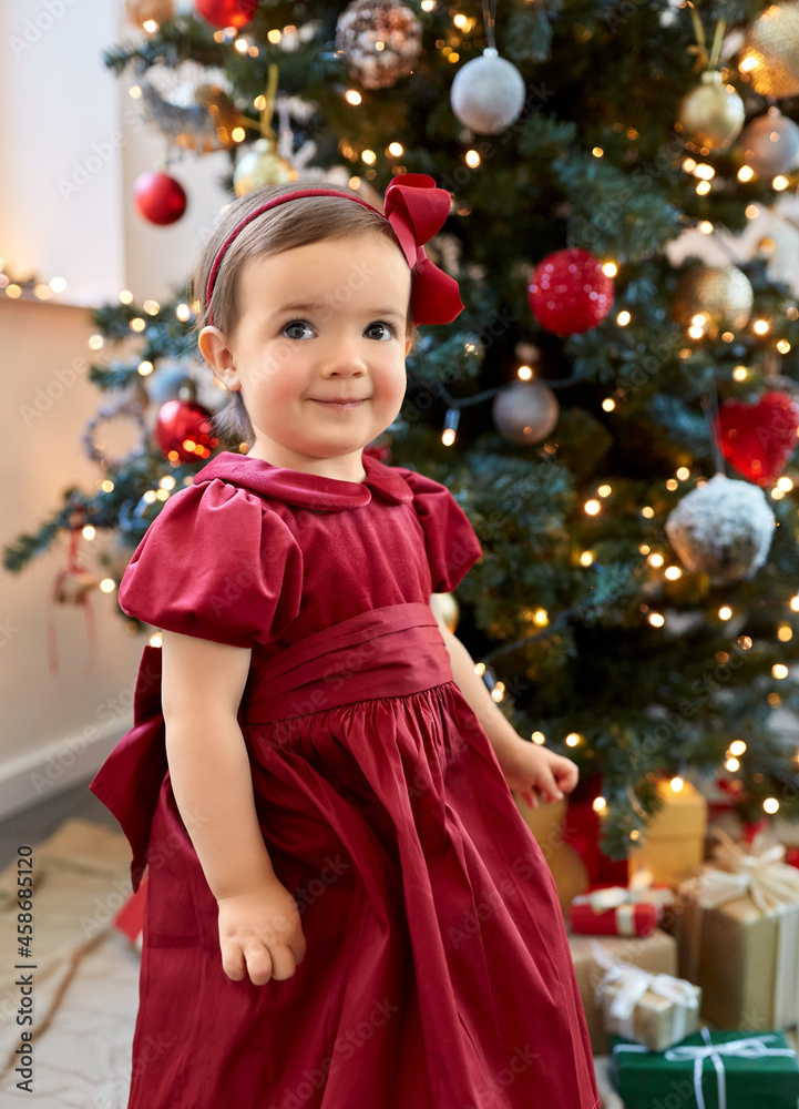 winter holidays and childhood concept - lovely baby girl in red dress over christmas tree at home winter holidays and childhood concept - lovely baby girl in red dress over christmas tree at home