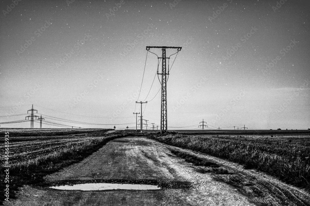 Grayscale shot of a country road and powerlines under a stary sky - obrazy, fototapety, plakaty 