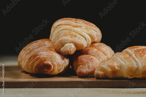 Freshly baked croissants on brown wooden table. Object on black background. Dark tone for food