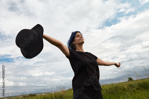 Calm woman spread her arms on sky are background. Closeup portrait young lady with flying blue hair. Concept of freedom, well being and lifestyle