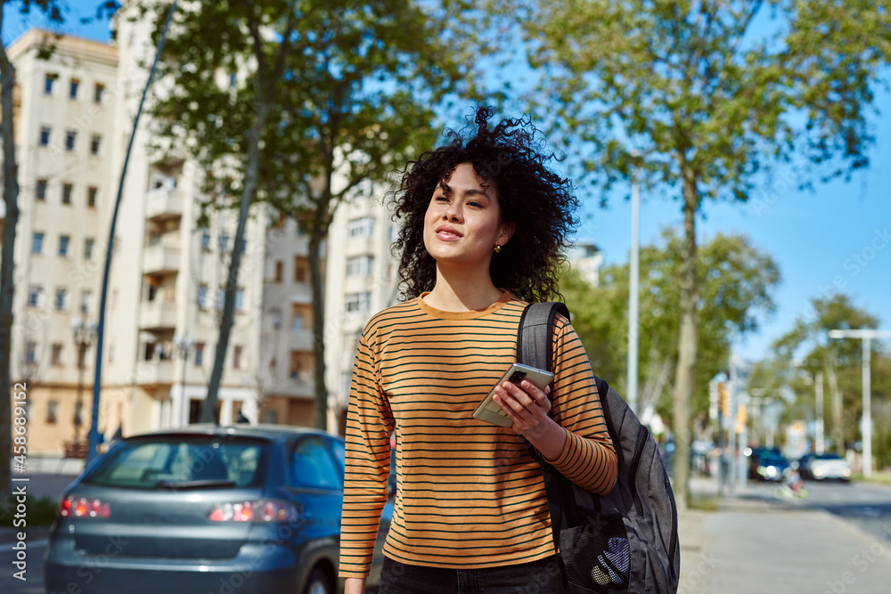 Fototapeta premium Cute young woman holding a cellphone while walking