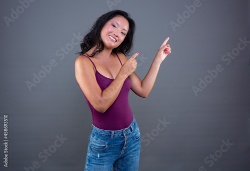 Young pretty long-haired brunette chinese extending her hand to the side to show or indicate something.