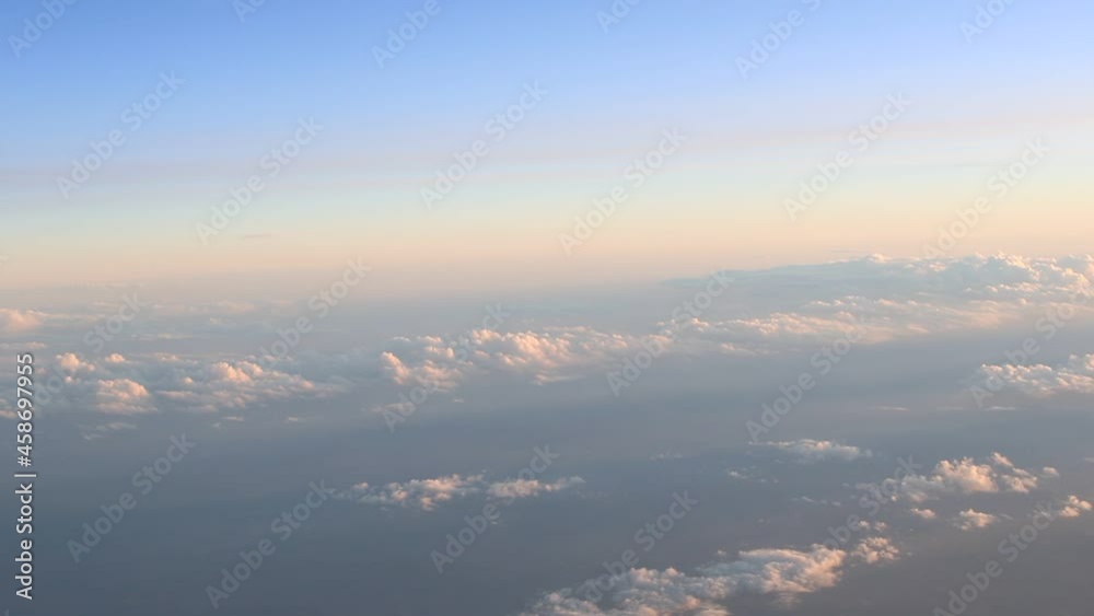 Above the clouds, sunset time, aerial view from the plane window, blue sky and clouds Above the clouds, sunset time, aerial view from the plane window, blue sky and clouds