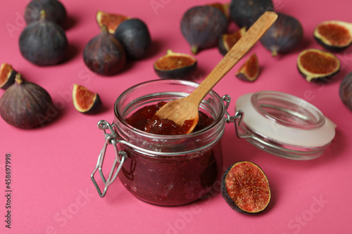 Jar with fig jam and spoon, and ingredients on pink background