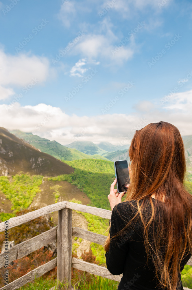 Young woman using smartphone to take a picture of a beautiful foggy mountains