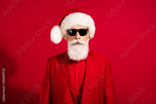 Portrait of attractive bearded grey-haired man wearing festal cap winter event festival costume isolated over bright red color background