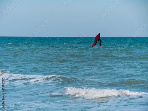 The athlete riding a hydrofoil surfboard using a hand held foil wing on ocean waves. Autumn extreme sport. Fall sea vacation fun. Windy weather on the beach.