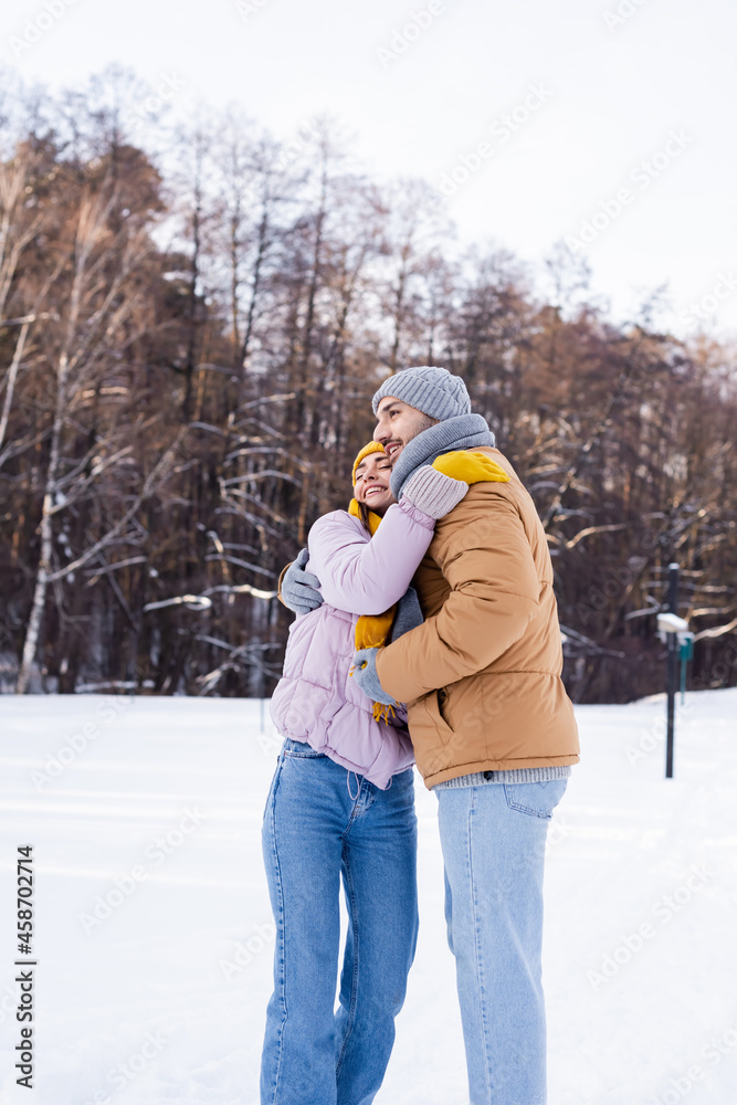 Smiling couple in warm clothes hugging in park with snow Smiling couple in warm clothes hugging in park with snow