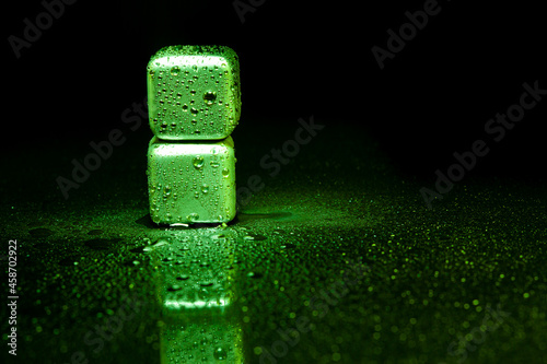 Fototapeta Naklejka Na Ścianę i Meble -  Green stainless steel cubes simulating ice for cooling drinks on a black surface with a reflection.