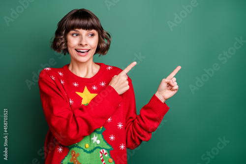 Photo of shiny excited young woman dressed red pullover smiling pointing looking empty space isolated green color background