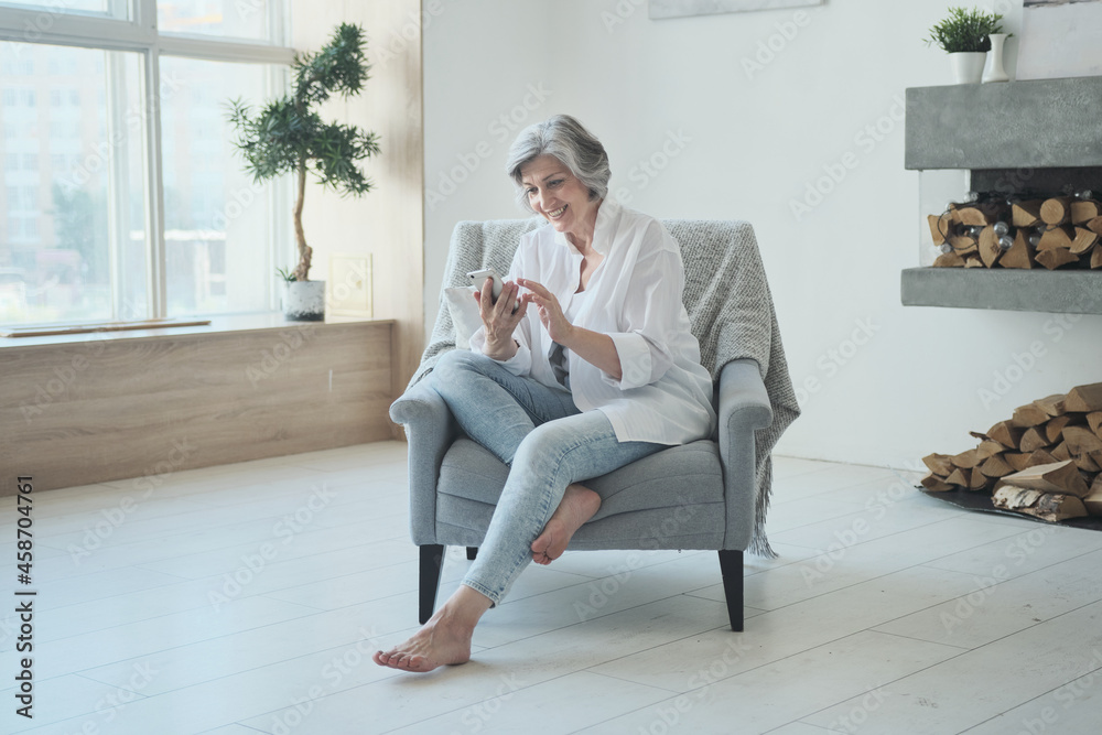 Senior woman looking at smartphone screen watching funny photo or video, modern grandmother enjoying online communication in social network web surfing or reading good comments and posts and smiling