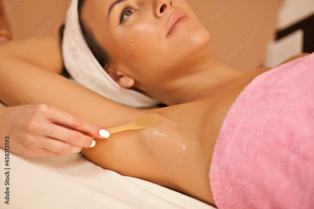 Beautician waxing female armpits in spa center