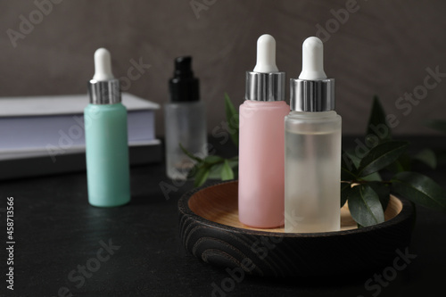 Bottles of serum on black table, space for text. Cosmetic products